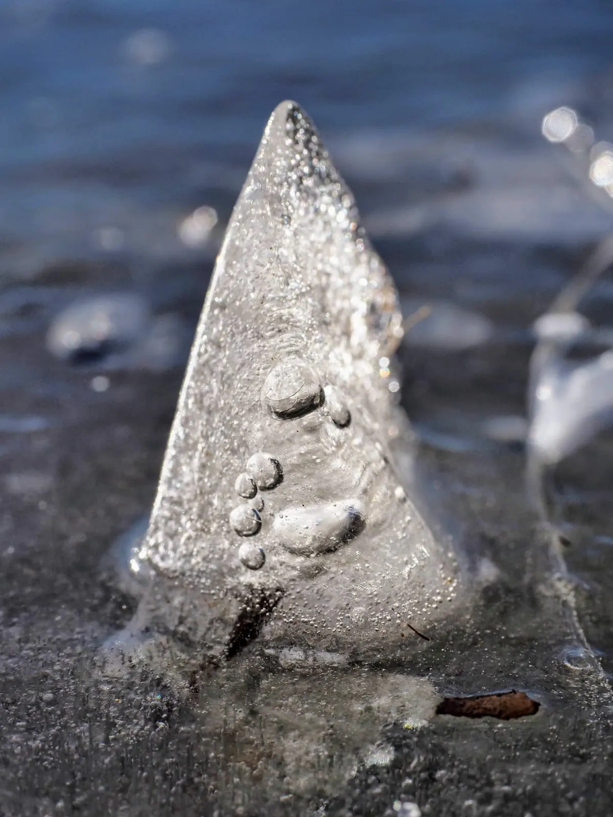 Cone of ice with bubbles standing on a frozen surface, 2021