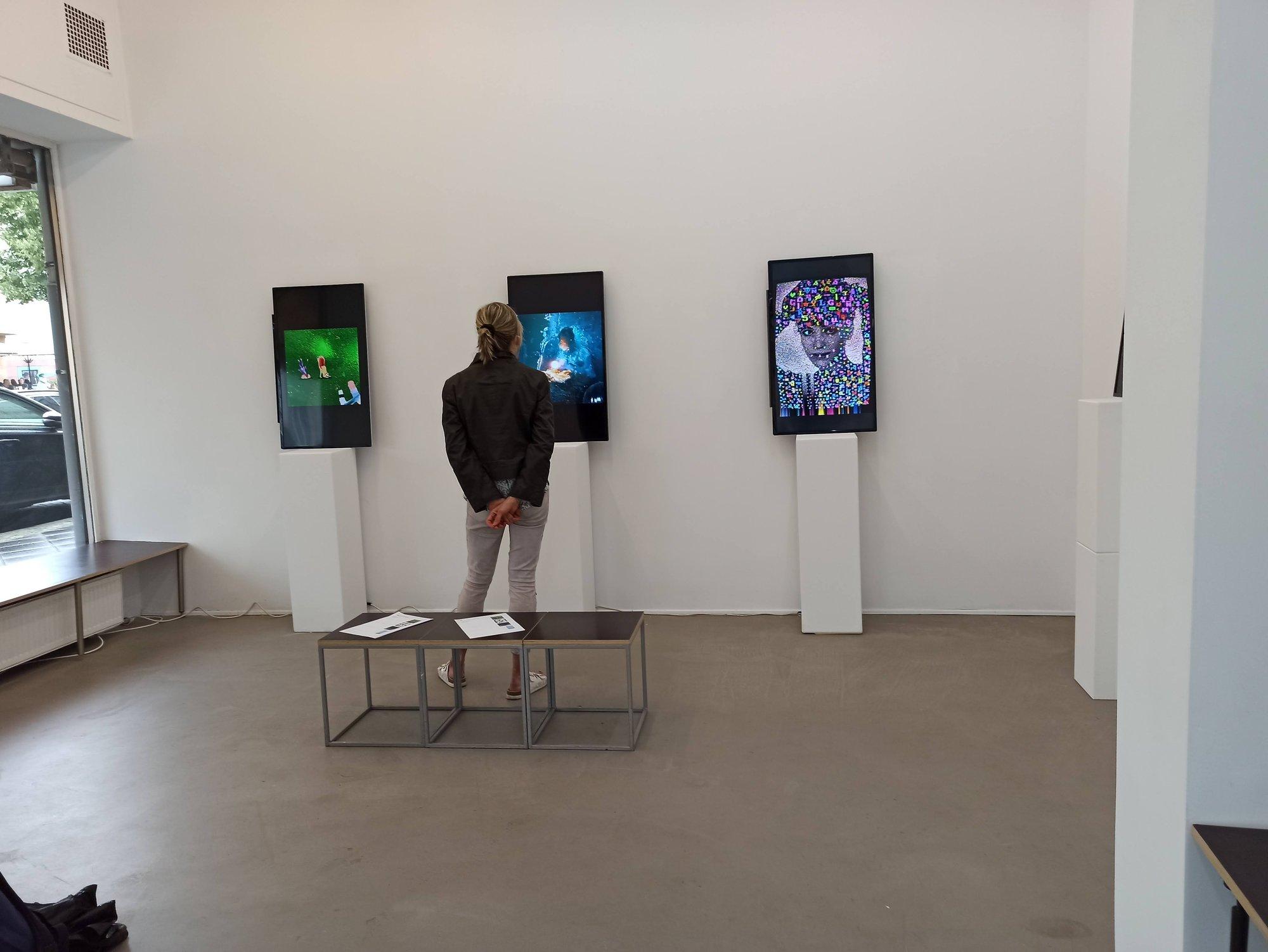 Eine Besucherin betrachtet drei bildschirmbasierte Arbeiten in der Galerie