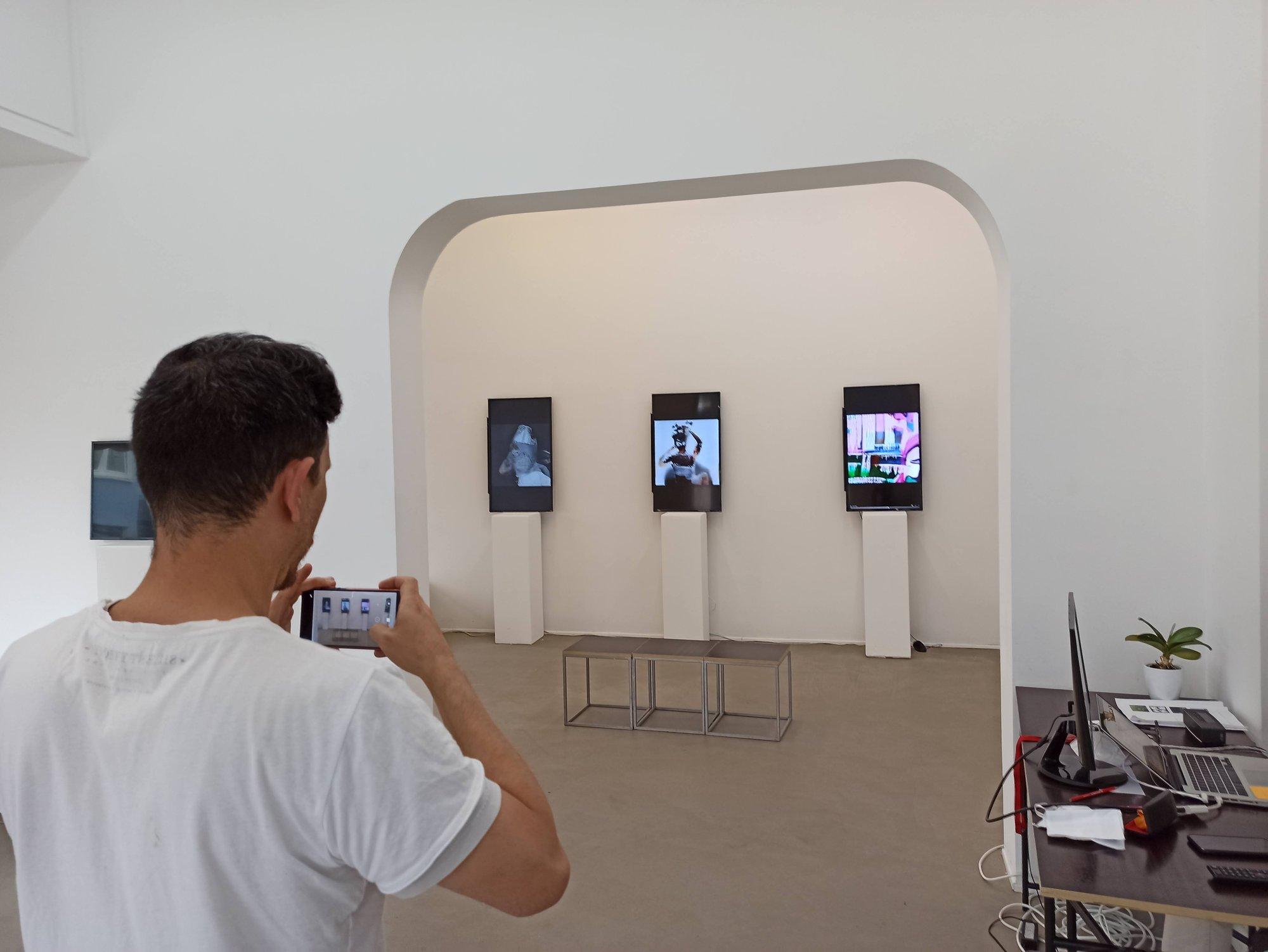 Ein Besucher fotografiert eine Reihe digitaler Arbeiten auf hochformatigen Displays
